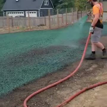 Worker spraying green hydroseed on residential lawn near custom home in Washington.