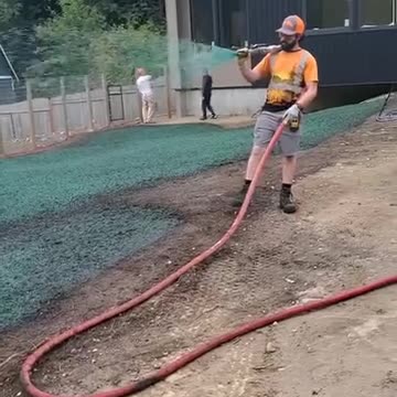 Man spraying green erosion control hydroseed on residential lawn site.