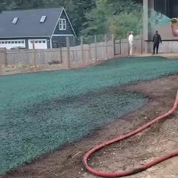 Hydroseeding application on residential lawn with two workers near wooden fence in Snoqualmie.