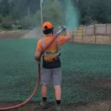 Technician spraying green hydroseed on residential lawn installation site.