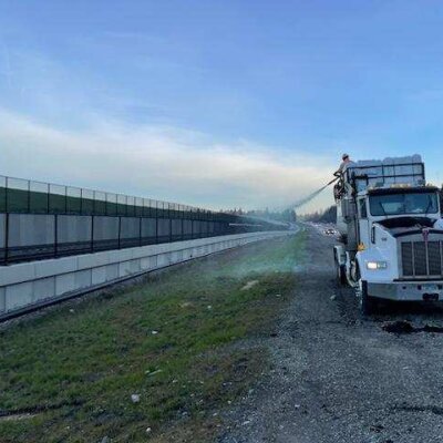 Semi-truck on roadside with person on top spraying water near highway at dawn.
