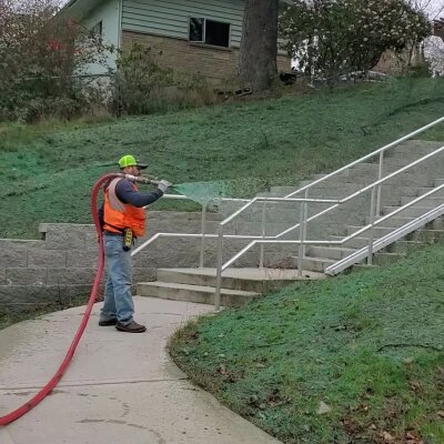 Worker spraying hydroseed on sloped lawn near stairs at residential property in Washington.
