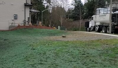 Grassy field with a cement truck and building in the background.
