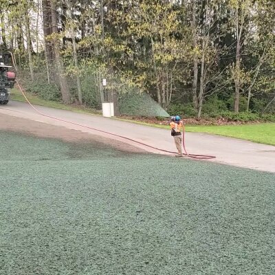 Person working with hose on artificial turf near trees.