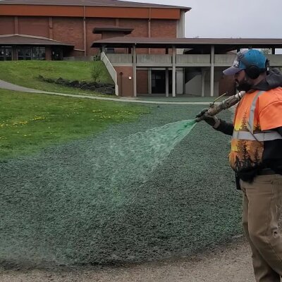 Worker spraying green hydroseed mixture on soil for grass growth.