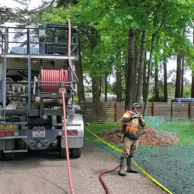Worker hydroseeding lawn with hose and truck in Washington state.