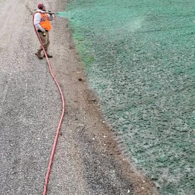 Worker applying hydroseed mixture to soil with hose in Washington state.