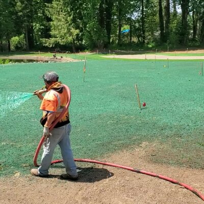 Worker hydroseeding lawn with green slurry in Washington State.