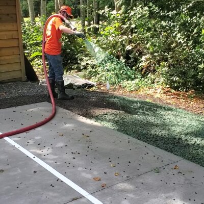 Hydroseed installer applying mixture on soil near concrete path.