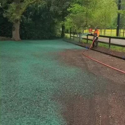 Worker hydroseeding lawn area near trees and fence in Washington State.