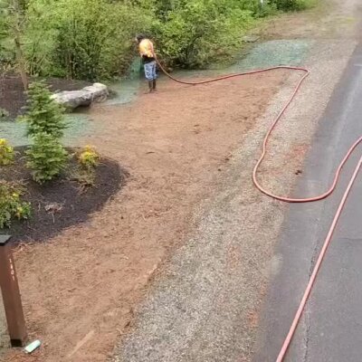 Worker spraying hydroseed on commercial landscape area near paved driveway in Washington.