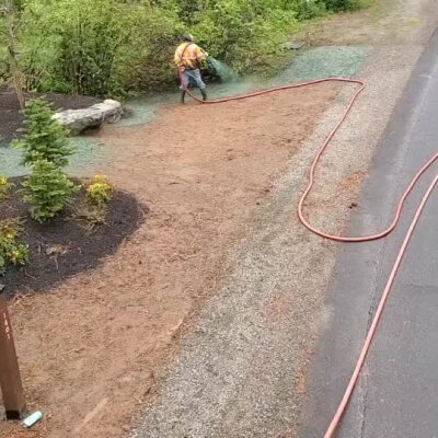 Worker spraying hydroseed on soil near landscaped area and roadside in Washington state.