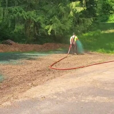 Worker applying hydroseeding on bare soil near wooded area in Washington State.
