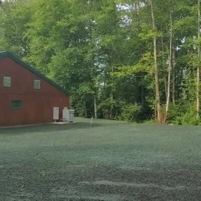 Freshly applied erosion control spray on soil near a red building and forest trees.