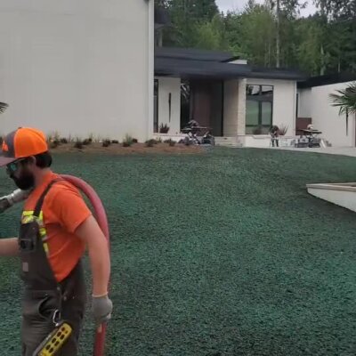 Worker applying hydroseed on front yard slope of modern high-end home.