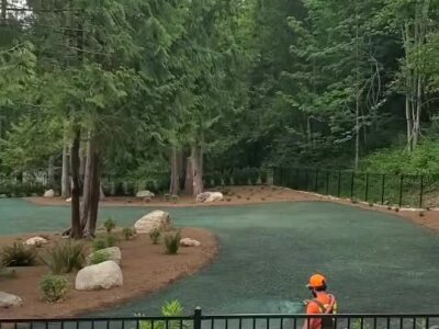 Hydroseed installation in wooded residential backyard with worker in bright safety gear.