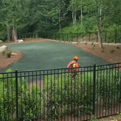 Worker applying hydroseed lawn in a residential backyard surrounded by trees and fencing.