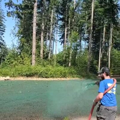 Man applying hydroseed lawn mixture near wooded residential area in Washington.