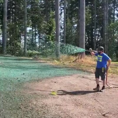Man spraying green hydroseed on bare ground near tall trees in Lake Stevens.