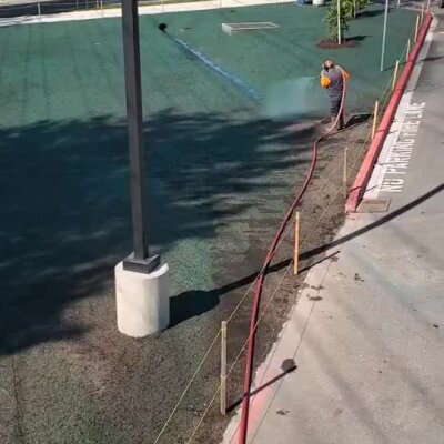 Hydroseeding worker spraying green grass seed and mulch on large school field in Bothell.