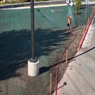 Worker applying hydroseeding on a large field near parking lot at Bothell elementary school