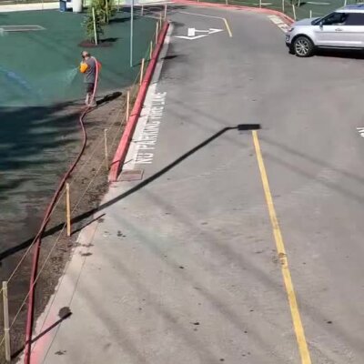 Man using hose to apply hydroseeding along school parking lot curb in Bothell, September 2025.